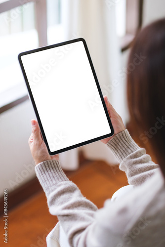 Vertical mockup image of a woman holding tablet with blank desktop white screen at home