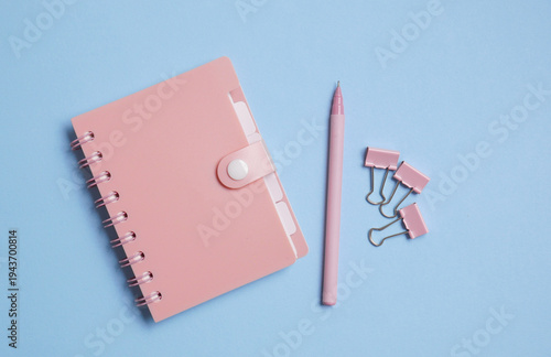 Pink notebook with pen and binders on blue background