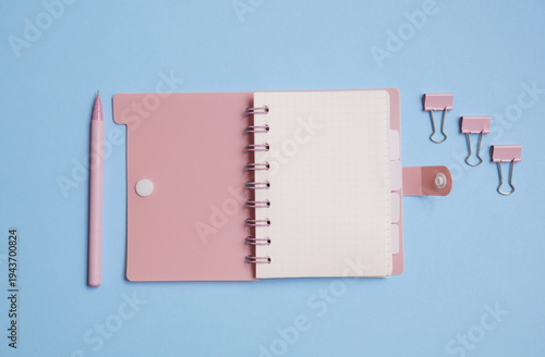 Pink notebook with pen and binders on blue background