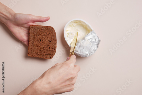 Hands spreading cheese on bread against a beige background. Snack, quick breakfast.