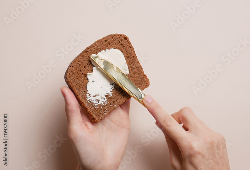 Foto Hands spreading cheese on bread against a beige background