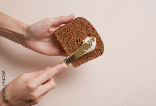Фотография Hands spreading cheese on bread against a beige background