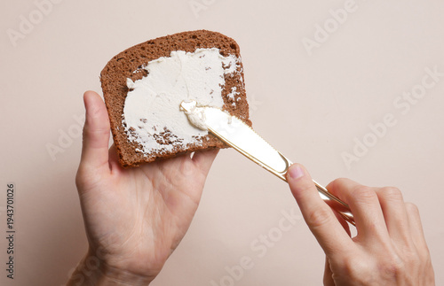 Tablou pe pânză Hands spreading cheese on bread against a beige background
