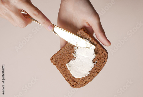Hands spreading cheese on bread against a beige background. Snack, quick breakfast.