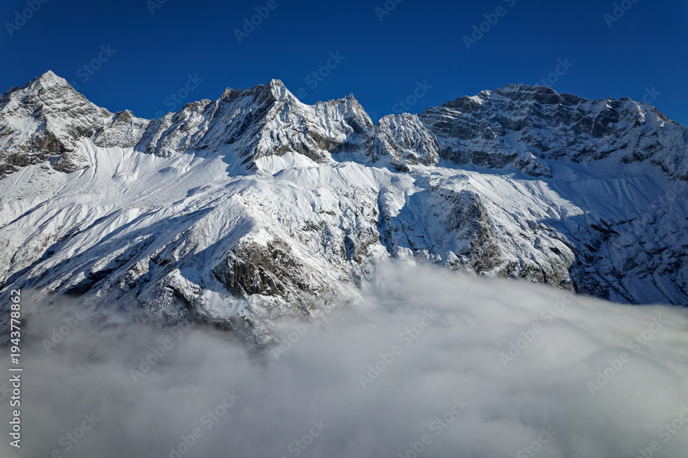Obraz premium Drone view landscape of Shuangqiao Valley (Shuangqiaogou or Double Bridge Valley) in Mount Siguniang in Sichuan, China. Beautiful snow capped mountains over white clouds in sunny day.