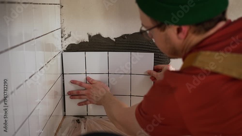 Careful young tiler pressing a sheet of white mosaic tiles onto fresh adhesive, performing a diy home renovation project to update his kitchen backsplash and save money