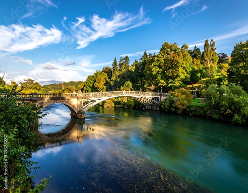 A serene river scene with a bridge surrounded by lush greenery and a blue sky