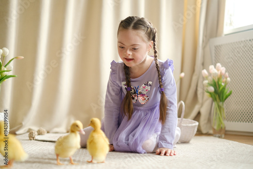 A girl with Down syndrome lies on the carpet at home, smiling and watching cute ducklings in the soft spring light. ??