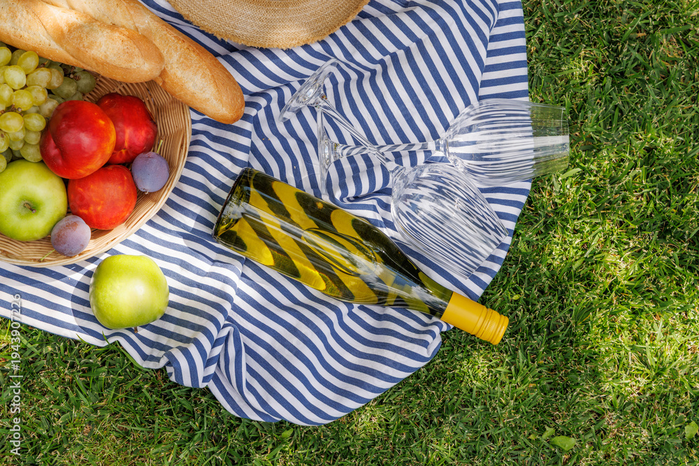 Fototapeta premium Picnic with wine, fruits, and baguette on a green meadow