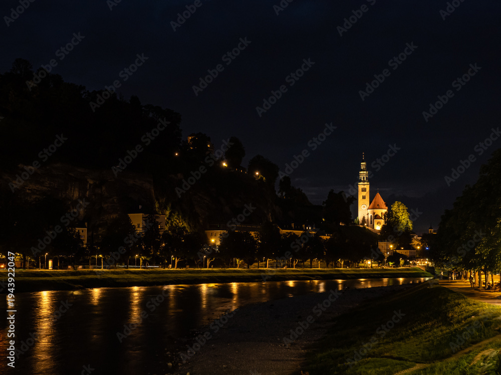 Obraz premium Night view of the city of Salzburg, Austria, highlighting the illumination of its historical monuments along the Salzach River