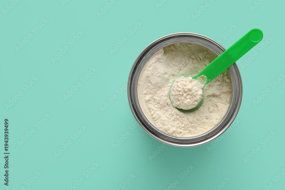 Fototapeta premium Jar of powdered baby milk formula with measuring scoop on turquoise background