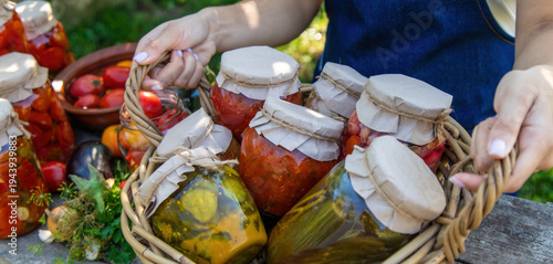 Φωτογραφία Woman holding wicker basket with jars of preserved vegetables on wooden table
