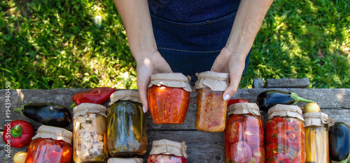 Farmer holding glass jars of preserved vegetables on wooden table in garden