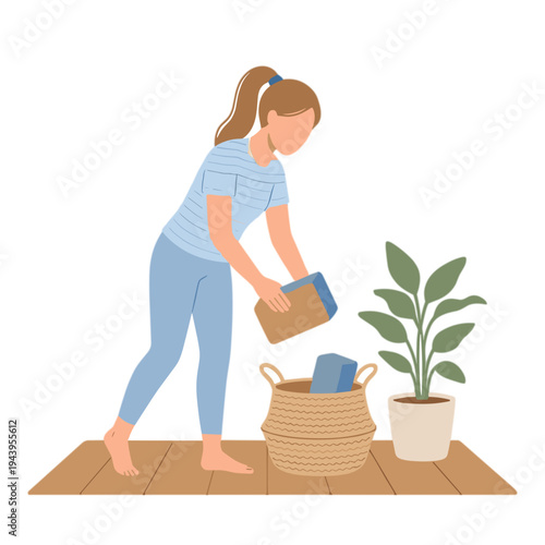 Woman putting folded clothes into a wicker basket on wooden floor next to plant