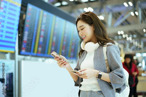 Happy Asian woman checking flight status on smartphone at airport