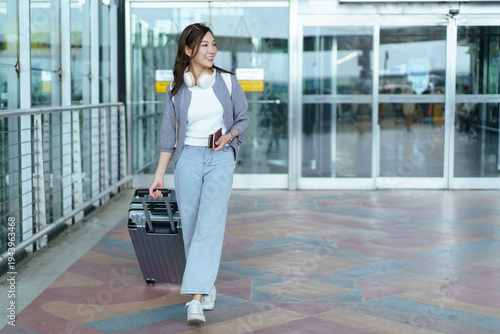 Happy Asian woman walking with suitcase at airport arrival