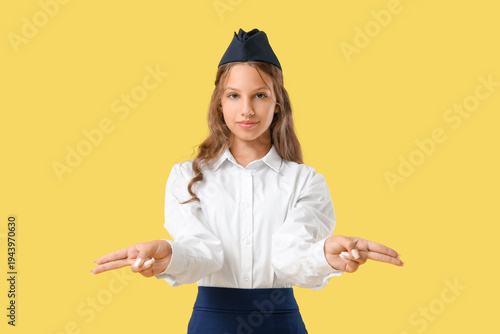 Cute teenage stewardess pointing at something on yellow background