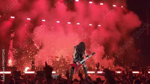 Rock Concert Spectacle - Guitarist Leaps Amidst Pyrotechnics and Red Haze, Energizing the Crowd.