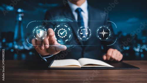 Businessman interacting with futuristic digital hologram interface with security checkmark scales and star icons floating above his hand with an open book on a wooden desk in a dark cityscape