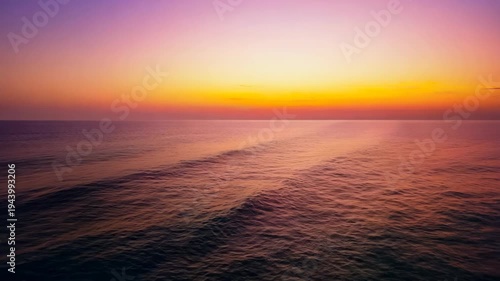 Serene ocean sunset with vibrant orange and purple hues reflecting on calm water surface, showcasing gradual color transition across the horizon