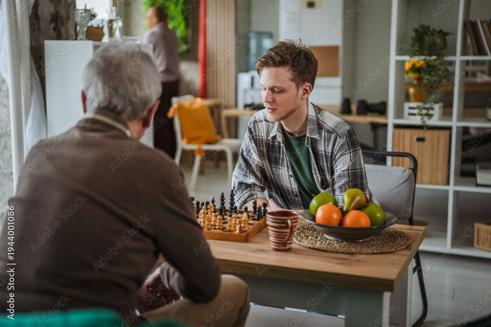 Fototapeta premium Young generation man playing chess with senior person