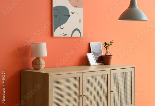 Chest of drawers with lamp, magazine and houseplant near orange wall in living room, closeup