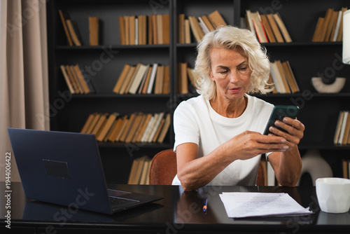 Obraz na plátně Confident stylish European middle aged senior woman using smartphone at workplace