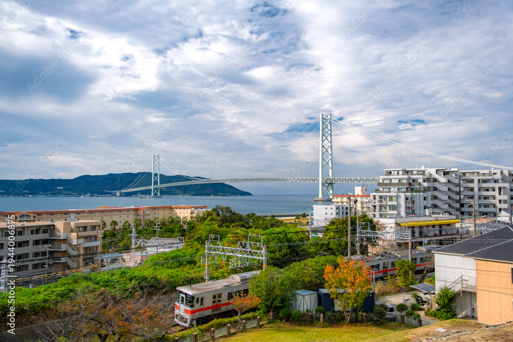 Obraz premium 兵庫県神戸市 明石海峡大橋と淡路島をバックに海沿いを走る山陽電車の風景