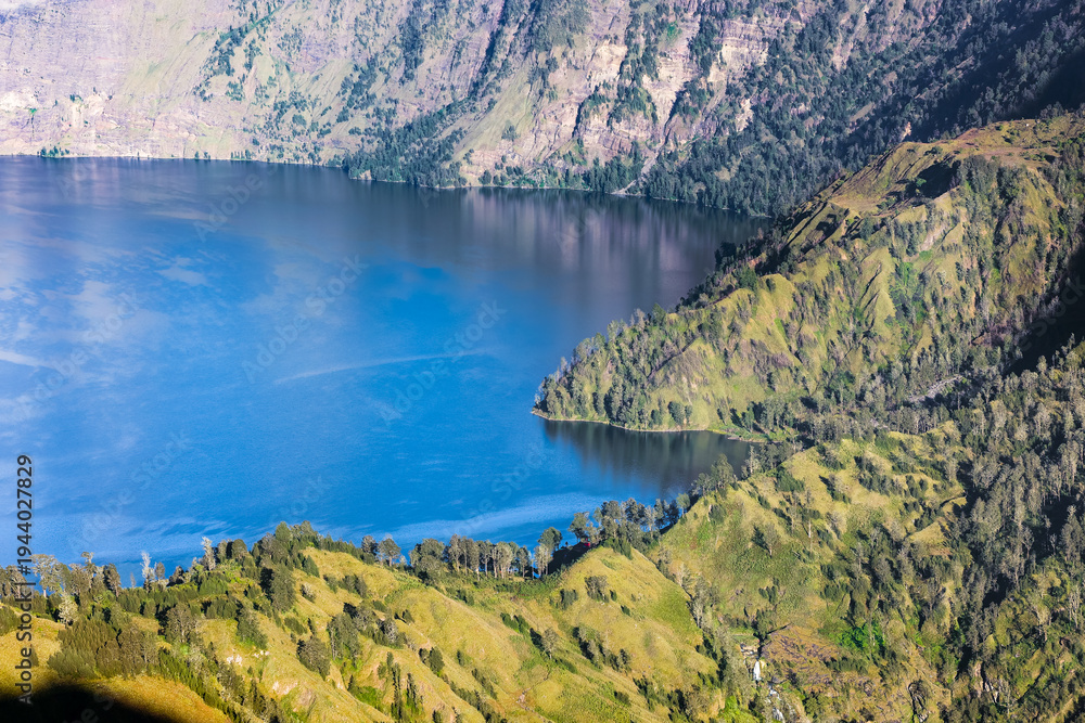 Fototapeta premium High angle view of Segara Anak lake surrounded by steep green crater walls of Mt Rinjani