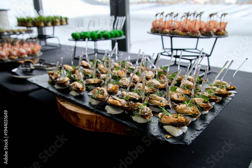 Gourmet mussels with microgreens served on a slate tray at a professional catering buffet. Luxury seafood appetizers for corporate events and wedding receptions with empty space for text.