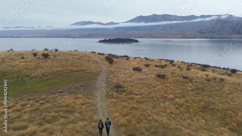 Aerial drone view of hikers walking trail above Lake Tekapo with mountains in Canterbury New Zealand
