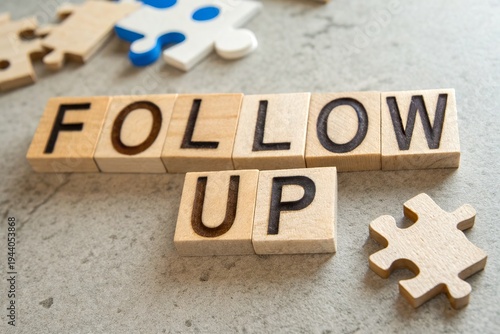 Wooden blocks spelling 'FOLLOW UP' on a textured surface with scattered puzzle pieces in the background