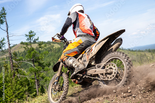 Close-up enduro rider on an dirt bike aggressively accelerating up rocky mountain slope, rear wheel spinning and flinging dirt and stones