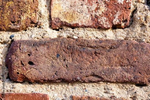Textured brick wall with various shades of red and brown. The surface shows signs of wear and age, highlighting the rustic appearance of the bricks.