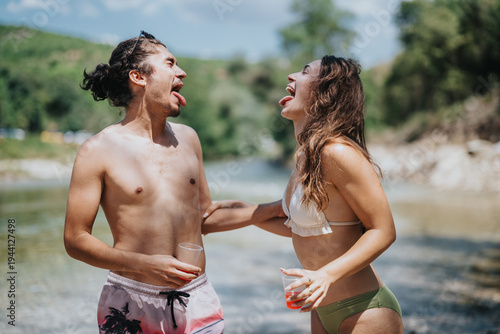 Obraz na płótnie Two friends in swimwear laugh and stick out their tongues by a river