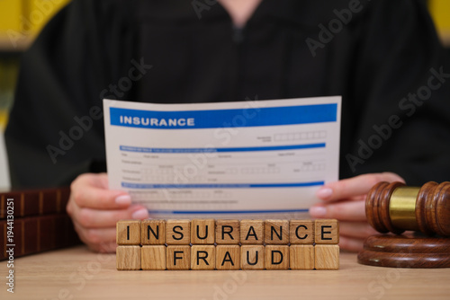 Konstfotografi In a solemn courtroom, a judge reviews a document concerning insurance fraud while wooden blocks spelling insurance fraud are displayed prominently