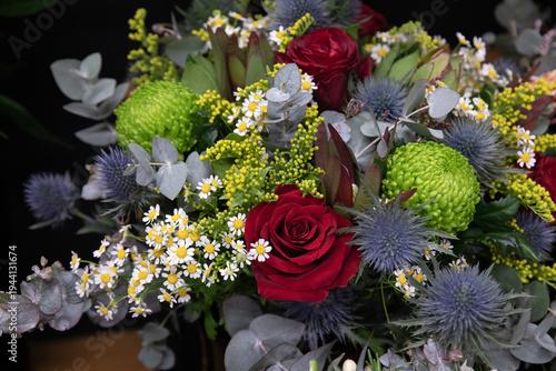 Bouquet with red roses, chrysanthemums and greenery in florist shop during day.