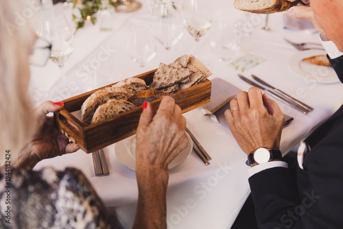 Fotografi Elegant senior couple sharing a wooden bread basket during a formal dinner party or wedding reception
