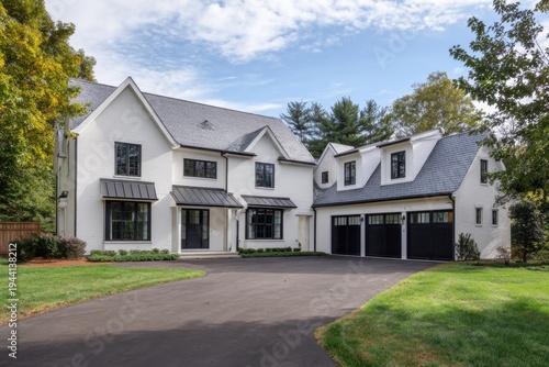 A spacious white house adorned with numerous windows and featuring a garage is situated in a peaceful suburban neighborhood, all under a beautiful blue sky.