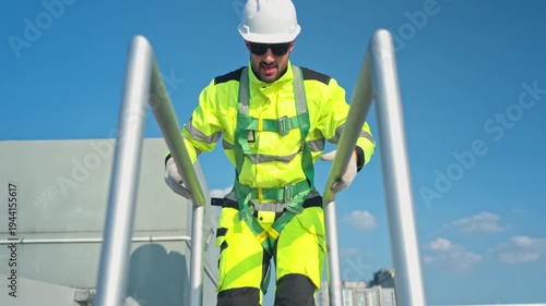 Young man engineer climbing a metal ladder to inspect industrial equipment, emphasizing safety standards and maintenance operations