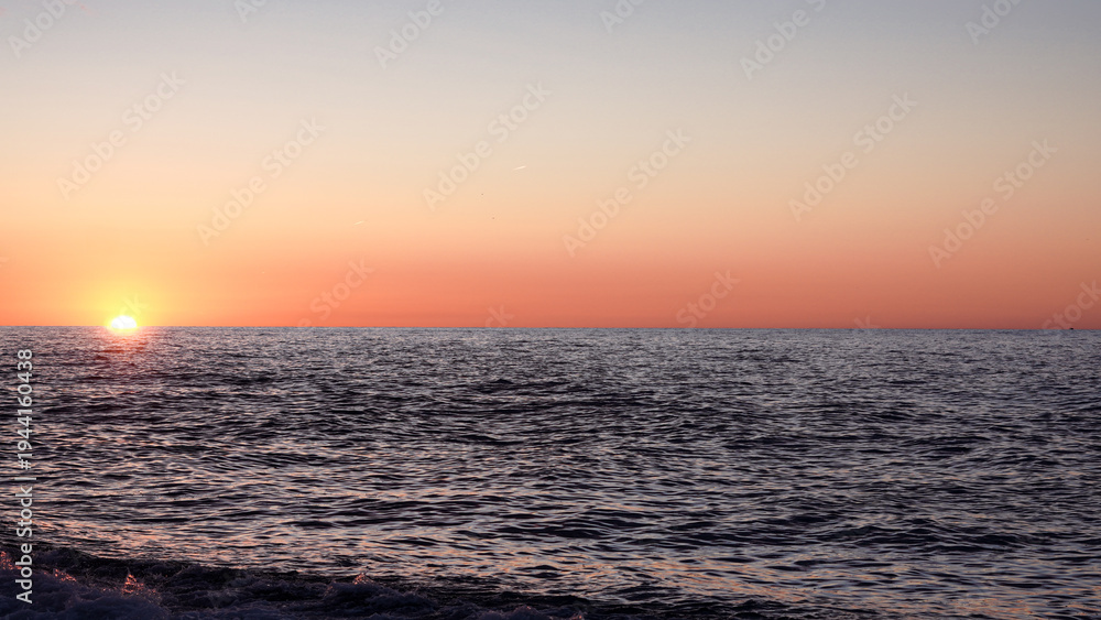 Obraz premium Sunset over calm ocean waters with colorful sky and gentle waves