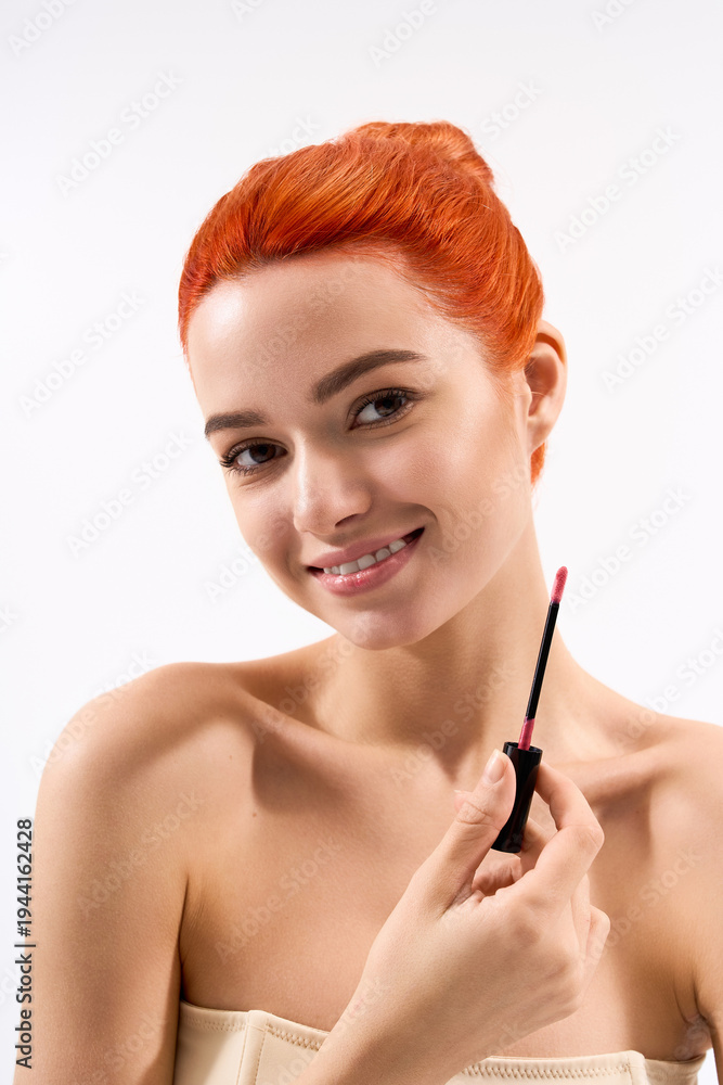 Fototapeta premium Stylish young woman applies lipstick with a confident smile in a bright setting