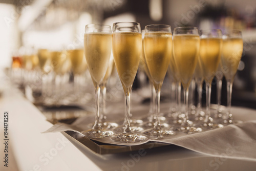 Elegant champagne flutes filled with sparkling wine on a silver tray with a white napkin. Professional catering at a luxury event, wedding, or gala dinner with a blurry sophisticated background.