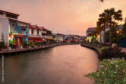 Sunset view of the Melaka River canal with colorful houses and murals in the historic center of Malacca, Malaysia.