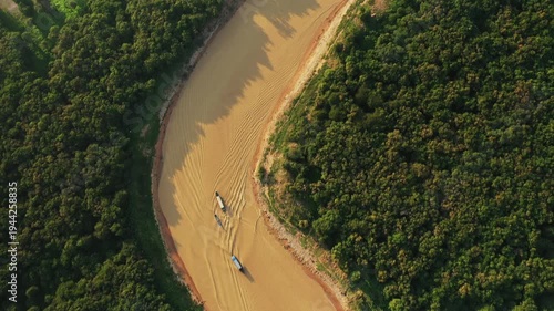Drone shot of muddy river winding through lush green forest near Chong Kneas, Cambodia, with boats traveling along the waterway.