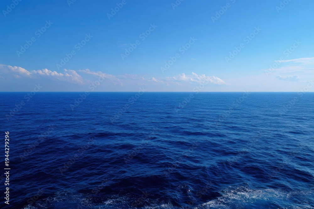 Fototapeta premium Deep calm blue ocean horizon under soft clouds with gentle swells and sparkling surface on a bright day