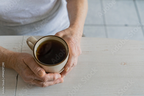 Senior person's wrinkled hands gently holding a hot mug of tea, finding comfort and warmth during a moment of relaxation