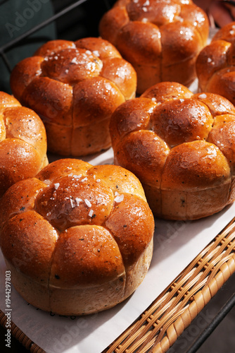 Baker Holding Tray of Fresh Brioche Buns with Sea Salt. A person holds a tray with golden brown, flower shaped brioche buns topped with sea salt, fresh from a professional bakery or restaurant kitchen