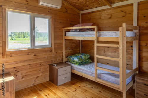 Clean and minimalistic summer camp room with bunk bed, white bedding, and a small wooden bedside table and large window. Cheap hostels, save money.