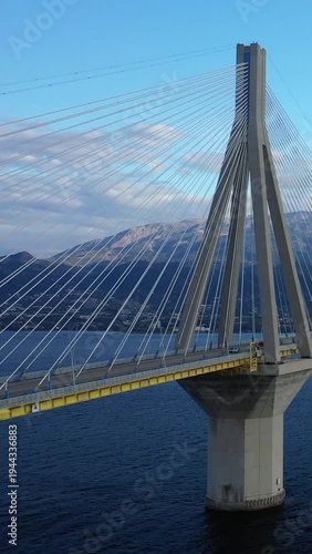 Close-up view of the Rion-Antirion Bridge spanning blue waters with mountains in the background under a clear sky in Greece.
